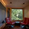 Baumhaus Lodge Schrems, © Niederösterreich Werbung / Maximilian Pawlikowsky Innenansicht einer modernen Baumhaus-Lodge mit zwei roten Sesseln vor einem großen Fenster mit Waldblick.