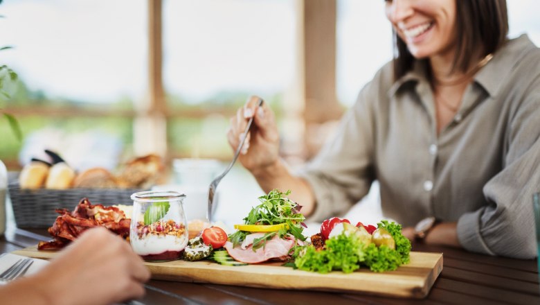 Terrace, © Waldivertel Tourismus, Gerhard Wasserbauer A woman eats breakfast with fresh ingredients on a wooden board on a terrace.