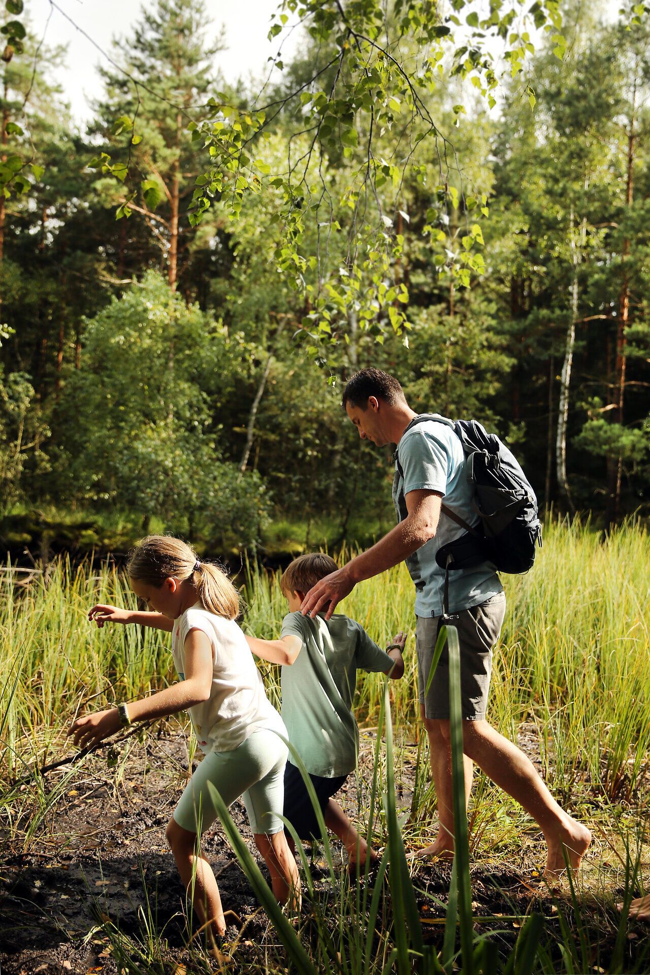 Eine Familie erkundet das Hochmoor, während sie durch das feuchte Terrain watet. Umgeben von üppigem Grün und der sanften Stille der Natur, erleben sie die Schönheit und Ruhe dieses einzigartigen Ökosystems. Die Kinder lachen und spielen, während sie die faszinierenden Pflanzen und die frische Luft genießen.