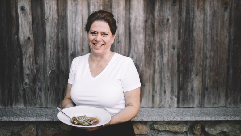 Frau mit wei&szlig;em T-Shirt h&auml;lt einen Teller mit Essen vor einer Holzwand.