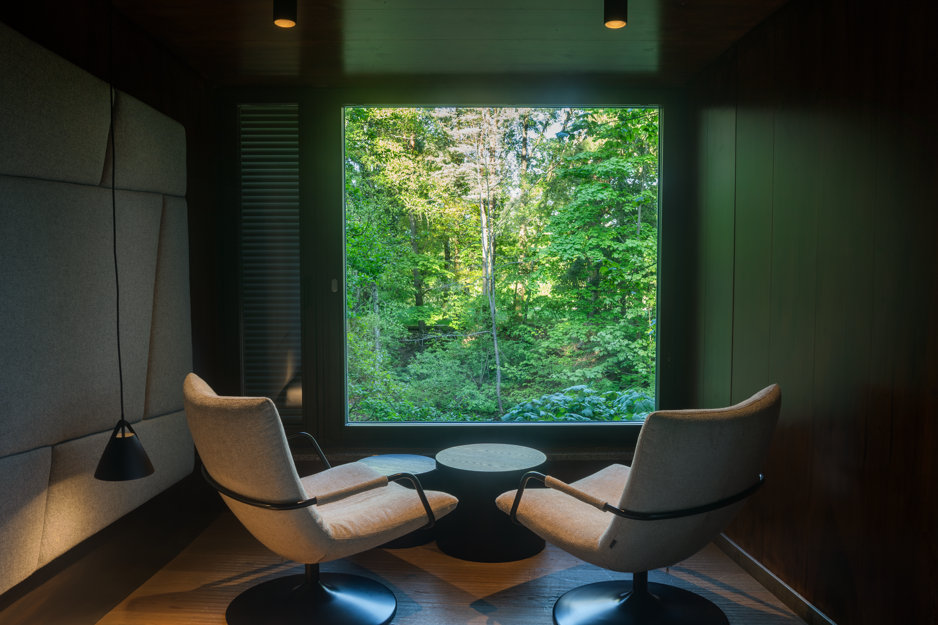 Innenansicht eines modernen Baumhauses mit zwei Sesseln und großem Fenster mit Waldblick.