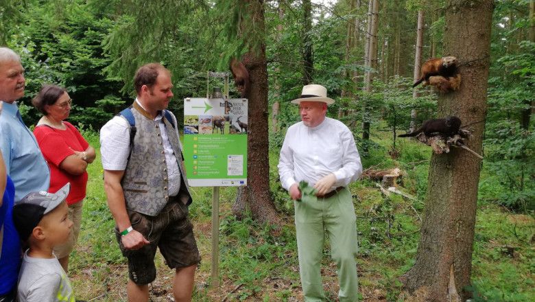 Gruppe von Menschen im Wald, die einem Mann zuhören, der vor einem Schild im Naturpark Geras steht.