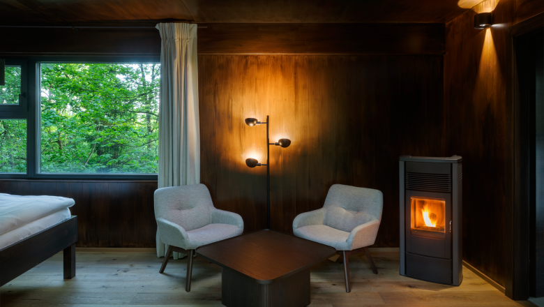 Innenansicht eines gem&uuml;tlichen Baumhauses mit zwei Sesseln, einem Tisch und einem Kaminofen.