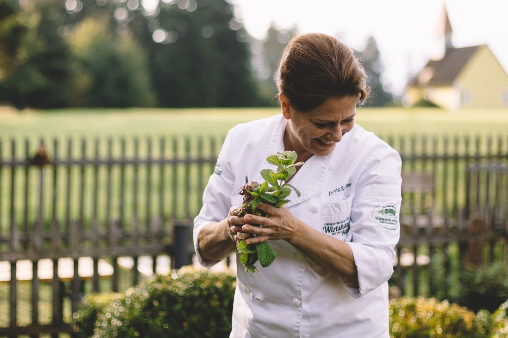 Eine Köchin in weißer Uniform hält frische Kräuter in einem Garten.