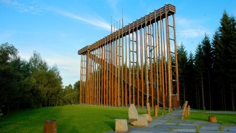 Eine hohe Holzkonstruktion im Freien, umgeben von Bäumen und grünem Gras.