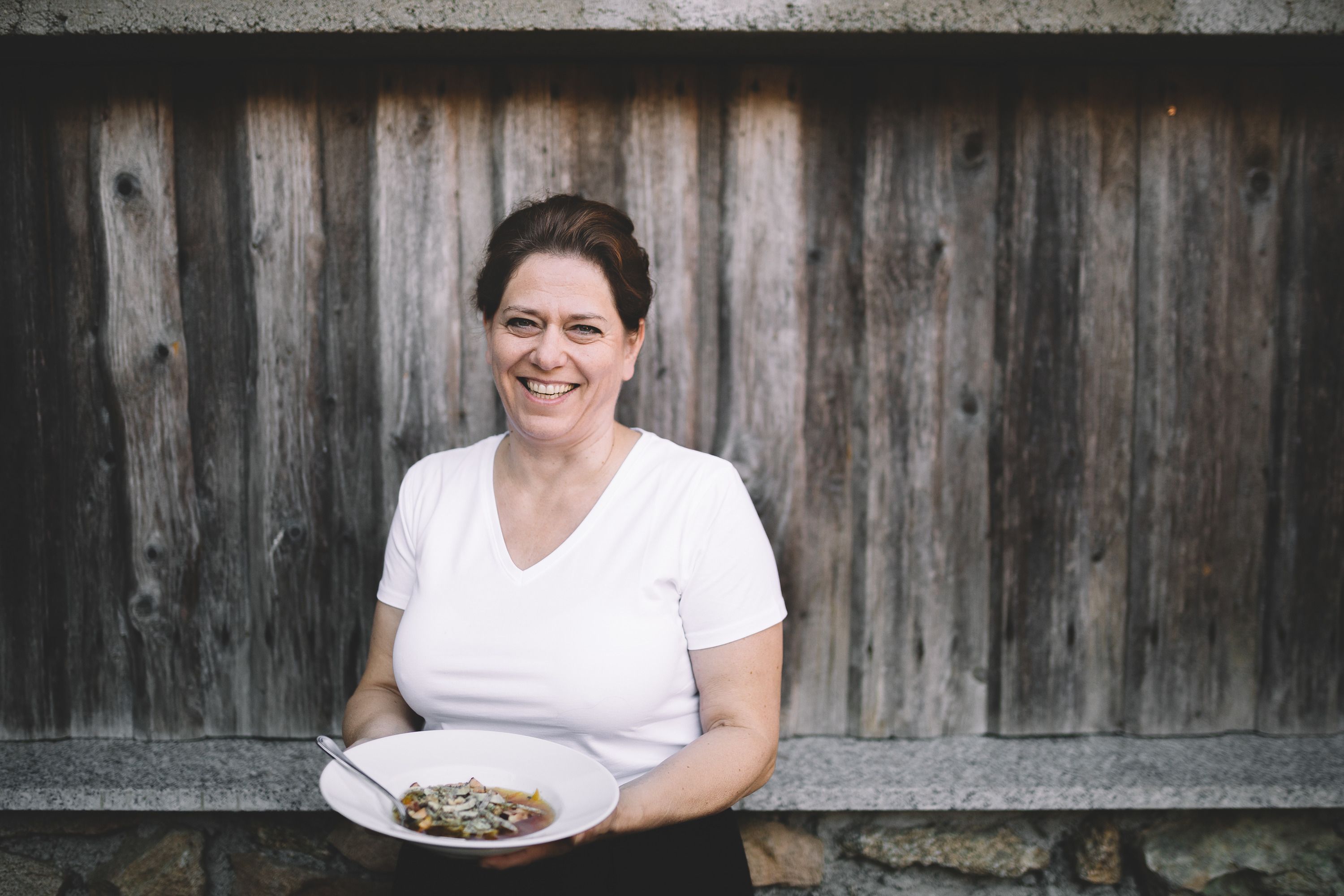 Frau mit weißem T-Shirt hält einen Teller mit Essen vor einer Holzwand.