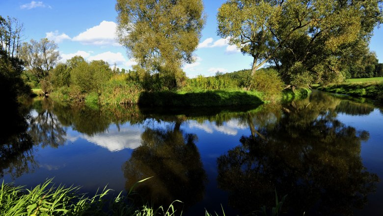 A calm river in the Dobersberg Nature Park with trees and blue sky in the background.