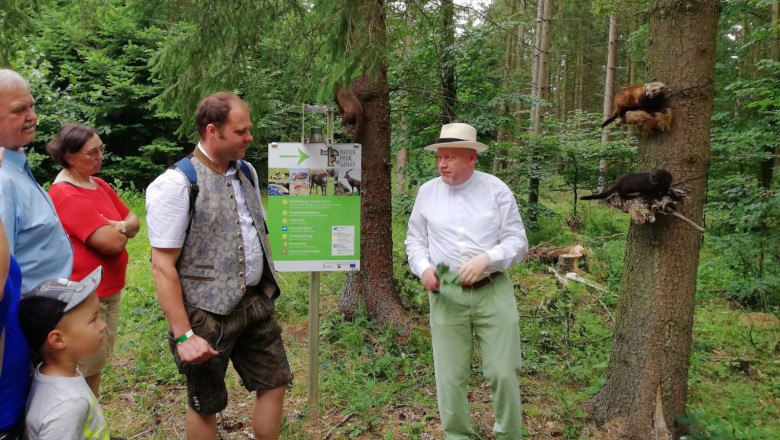 Gruppe von Menschen im Wald, die einem Mann zuh&ouml;ren, der vor einem Schild im Naturpark Geras steht.