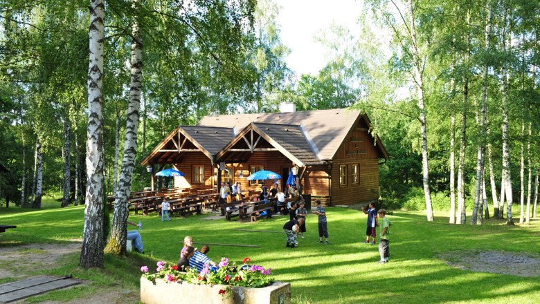 Holzh&uuml;tte im Naturpark Blockheide mit spielenden Kindern und B&auml;umen.