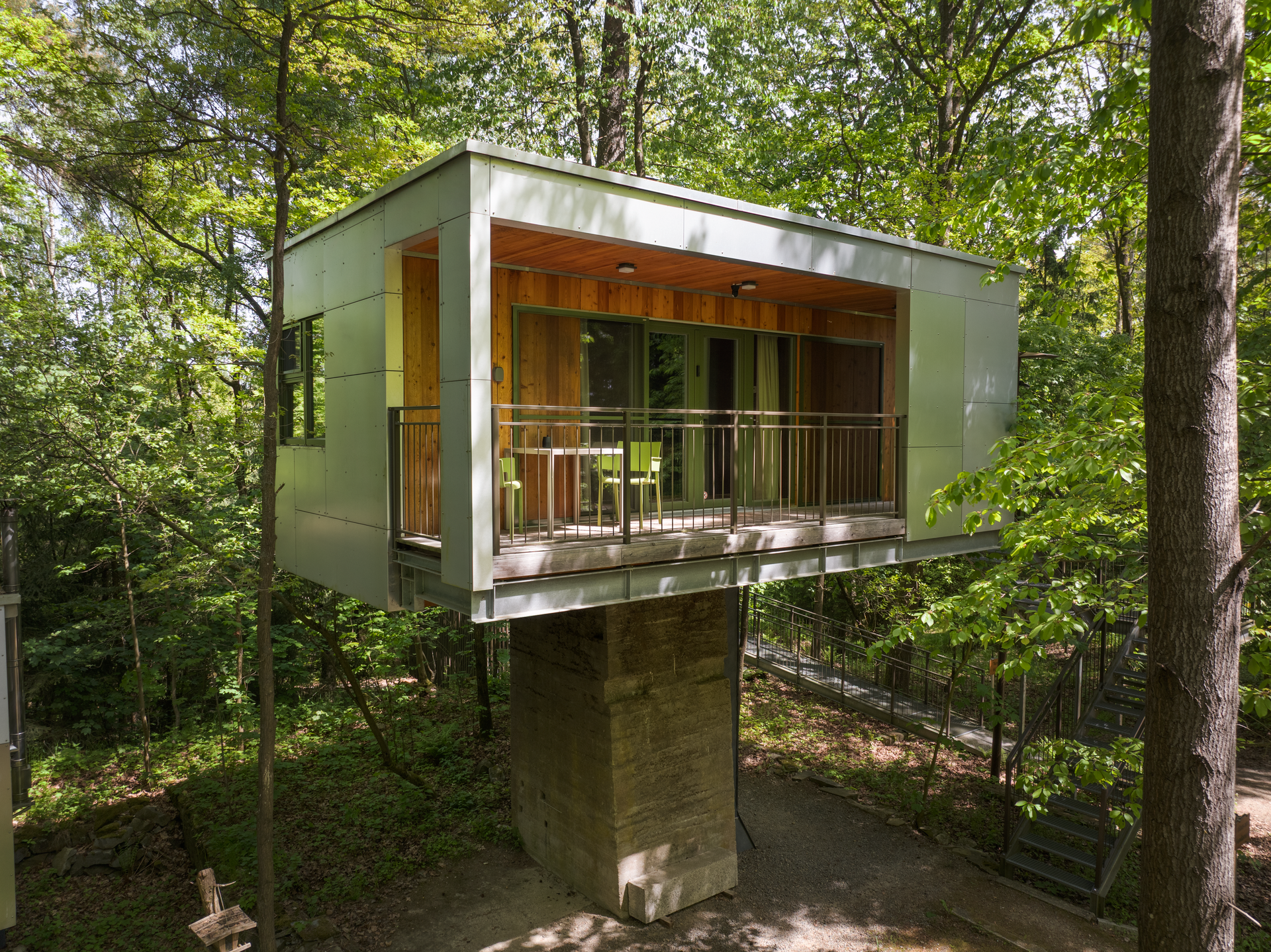 Modernes Baumhaus im Wald mit Balkon und Glasfront.