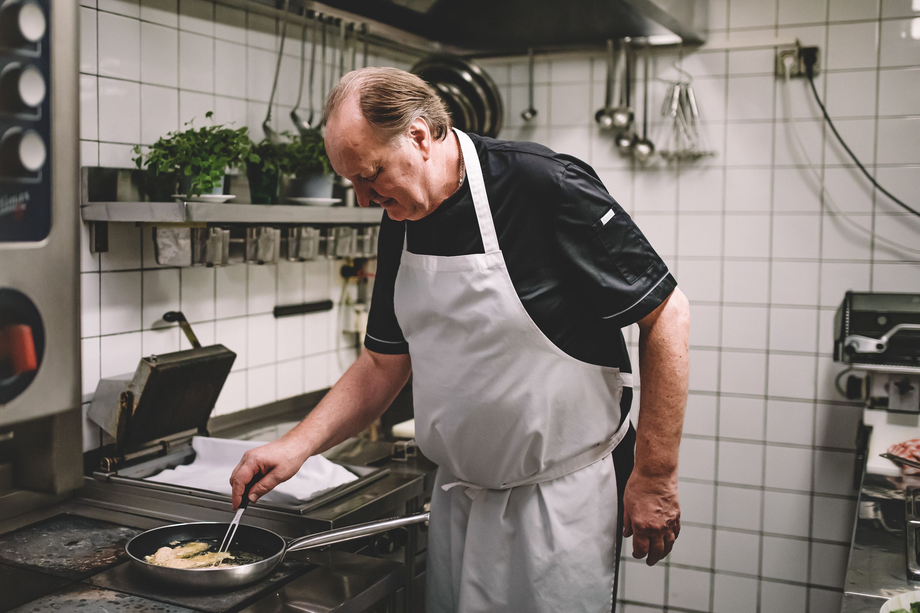 A cook in a professional kitchen is frying something in a pan.