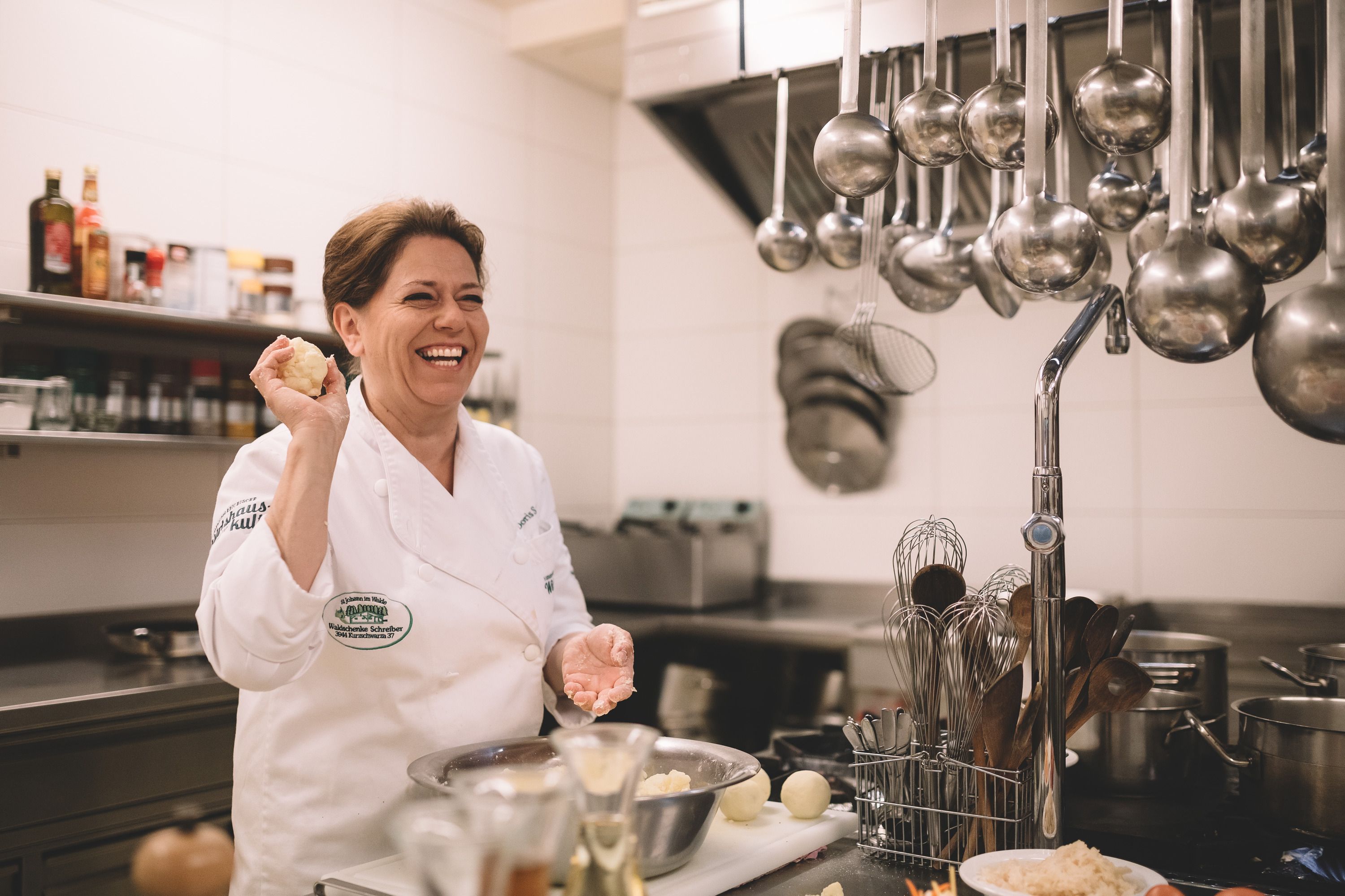 Eine lachende Köchin in einer professionellen Küche, die einen Teigball in der Hand hält.