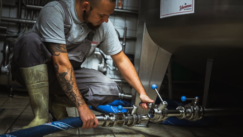 Muž v pracovn&iacute;m oblečen&iacute; drž&iacute; sklenice s pivem před pivovarem.