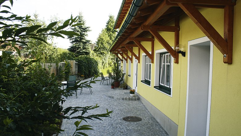Gepflasterter Hof mit gelbem Geb&auml;ude und Gartenm&ouml;beln.