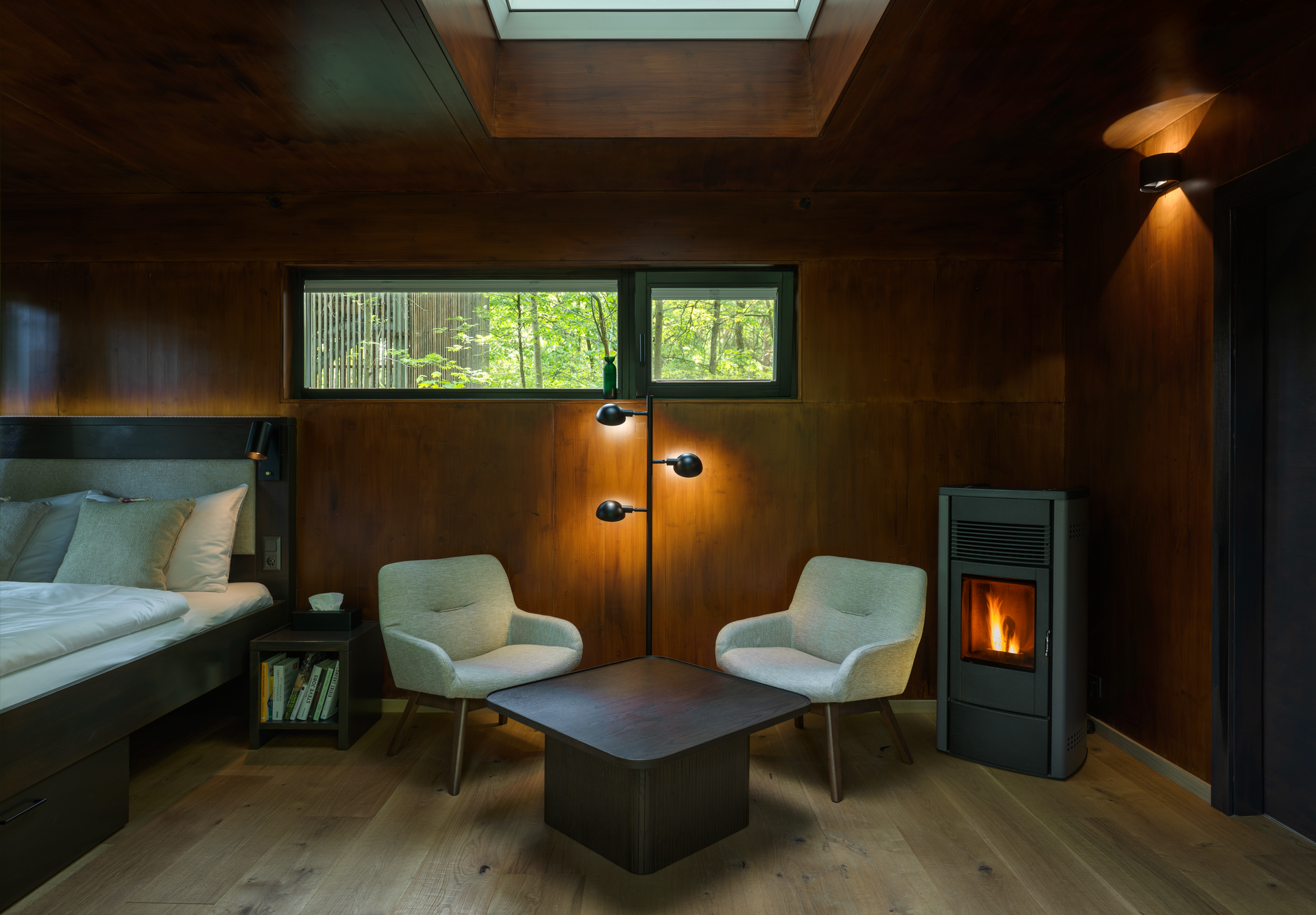 Innenansicht eines gemütlichen Baumhauses mit Holzverkleidung, zwei Sesseln, einem Tisch und einem Kamin.